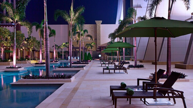 傍晚时分的池畔休息室，旁边是灯光照耀的泳池和棕榈树