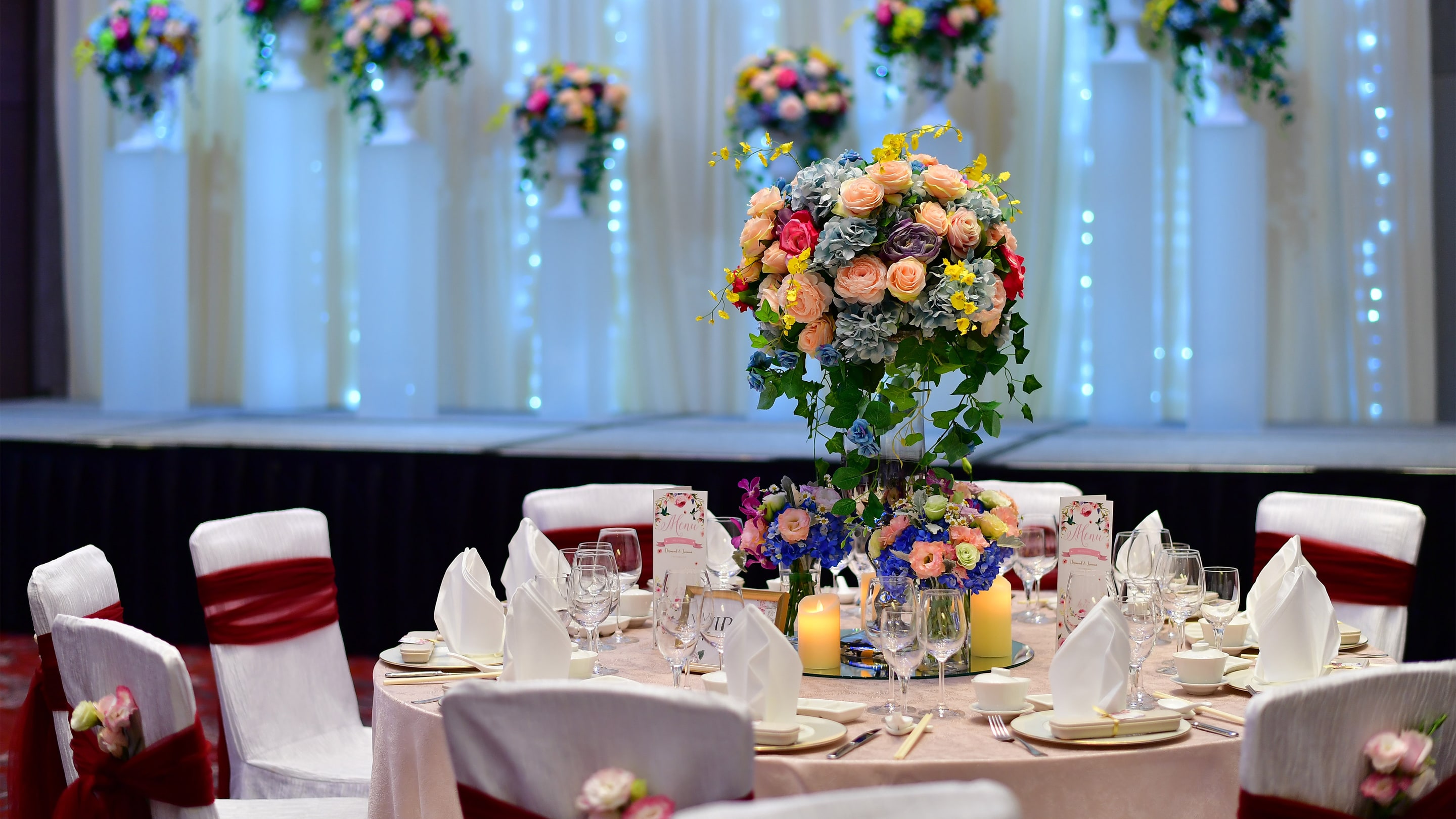 宴会厅内设靠墙花束和桌子，桌面摆设中央鲜花装饰。