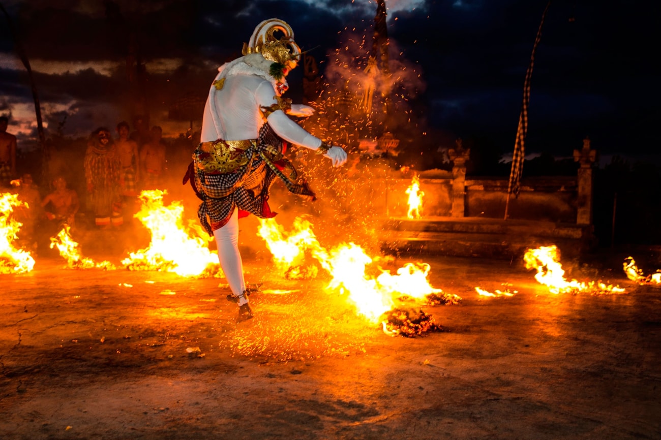 一位身穿白色紧身衣、头戴公羊面具的男士在夜间人群前跳起火焰舞