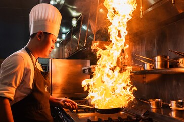 A chef cooking meat over an open flame grill.