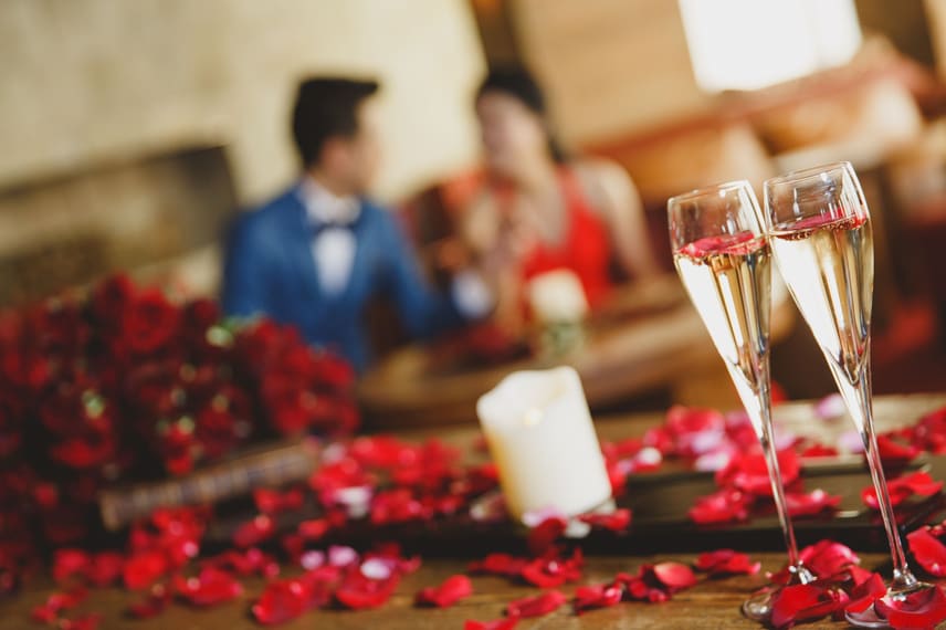 Two glasses of champagne, rose petals and a couple in the background