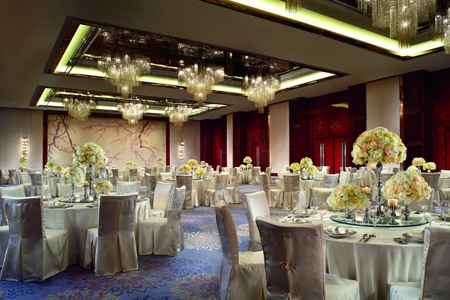 Large space with multiple chandeliers and round tables with formal place settings and floral centerpieces