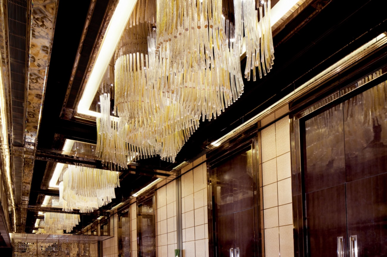 Hallway with large wood doors along one side, chandeliers and standing cocktail tables down the middle