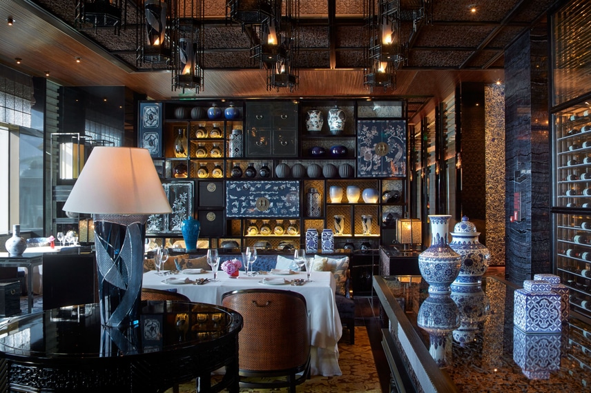 A dining room with a floor-to-ceiling shelf filled with traditional Chinese vases and a glass-enclosed wine room