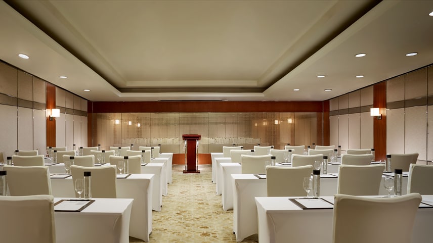 Meeting room with draped tables, draped chairs in two columns of multiple rows. 