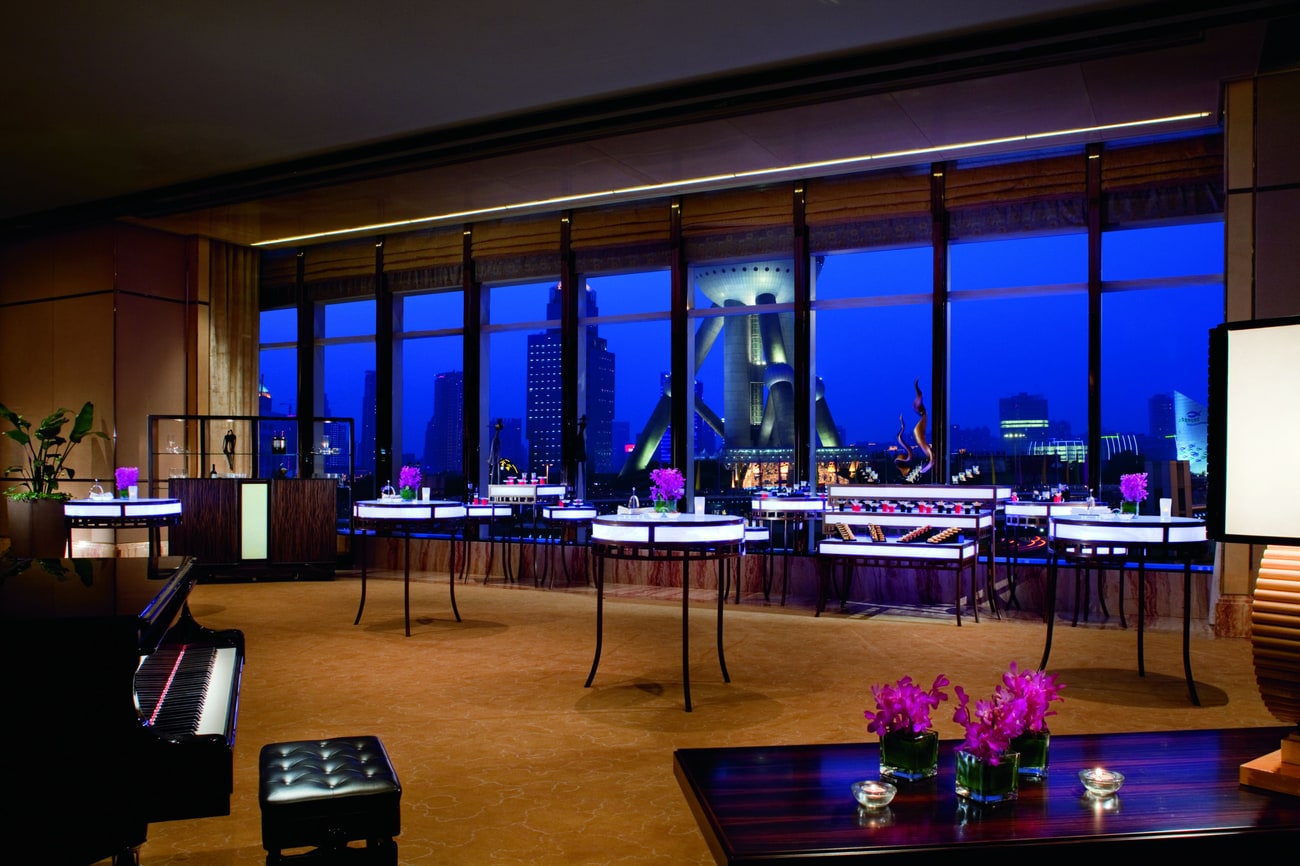 Illuminated cocktail tables and a piano complement the skyline evening views of a hotel function room