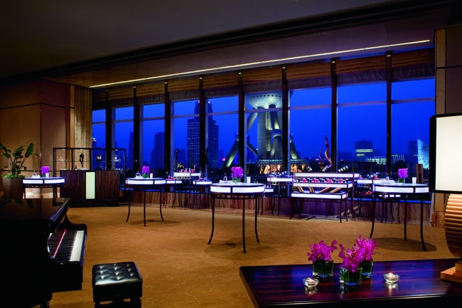 Illuminated cocktail tables and a piano complement the skyline evening views of a hotel function room