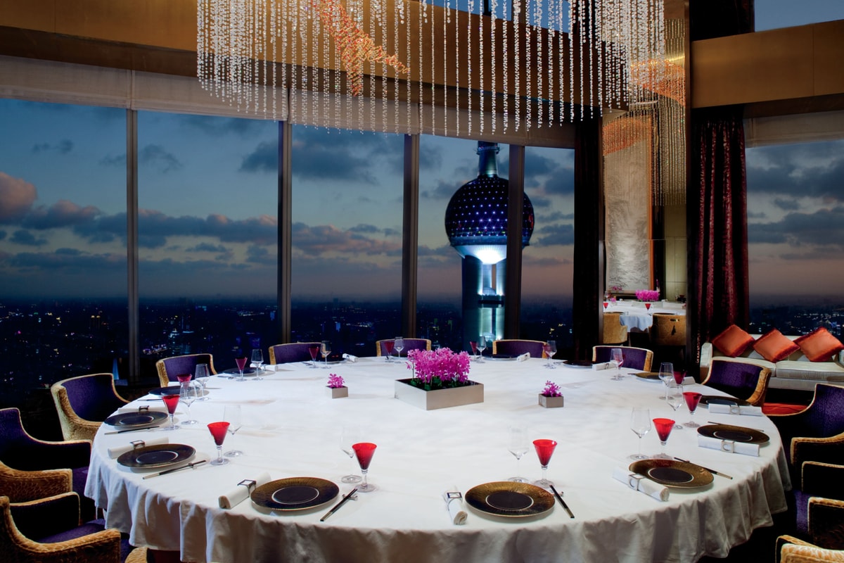 Expansive round table with panoramic evening views and an artistic light fixture featuring crystal strings and an orange fish
