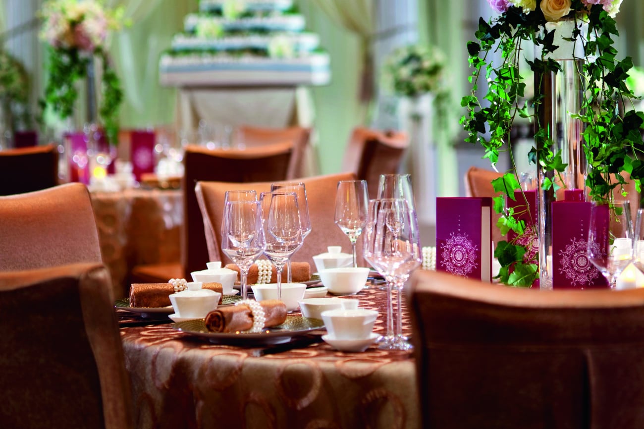 Wedding reception table with a cascading floral centerpiece, rust-colored linens and, in the background, a large cake