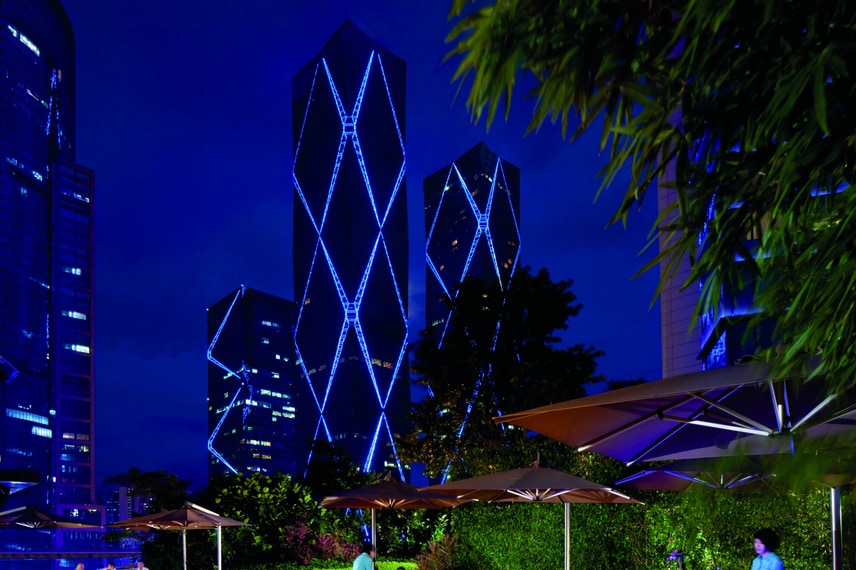 People sitting at tables with umbrellas on a patio at night with skyscrapers in the background