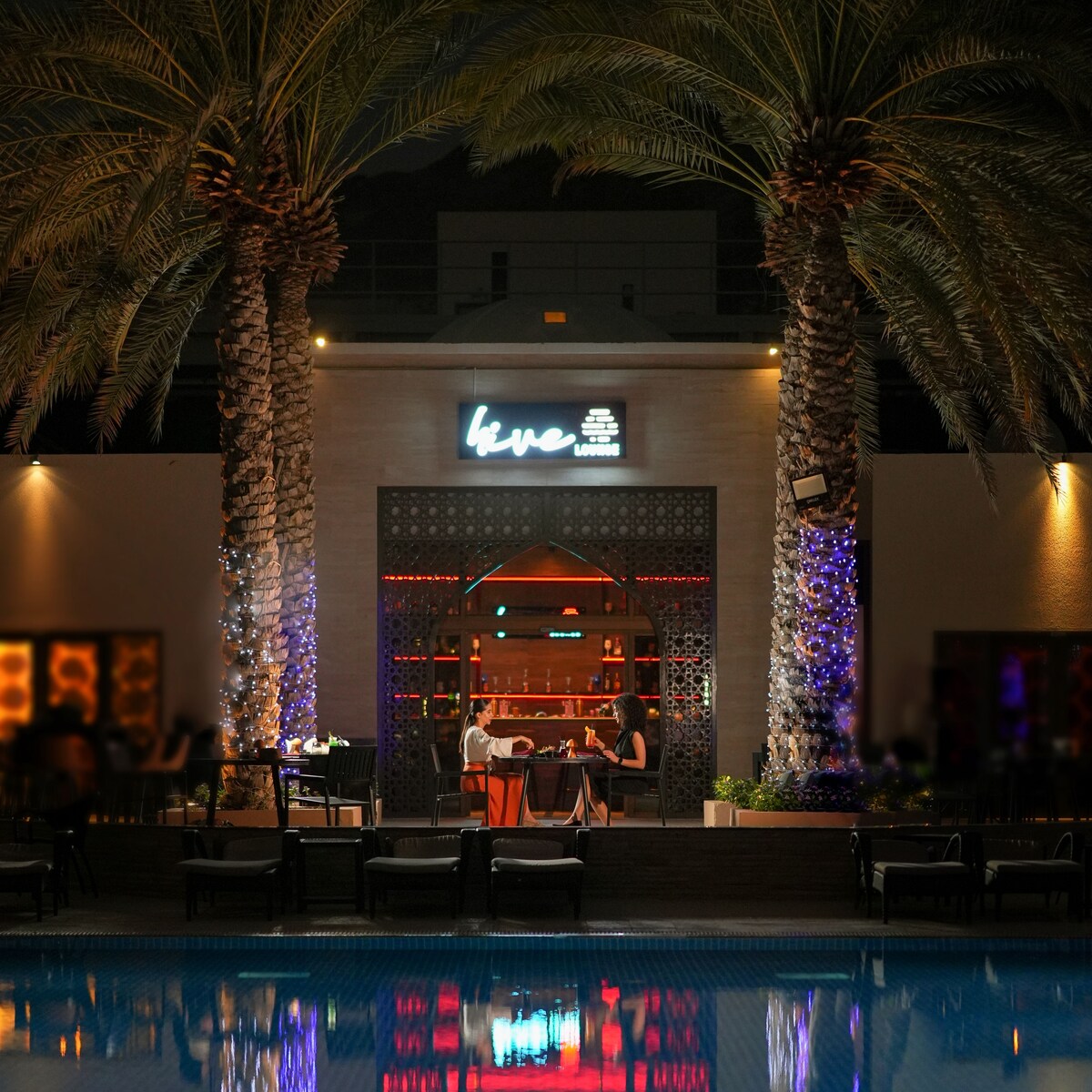two women at table by a pool at night