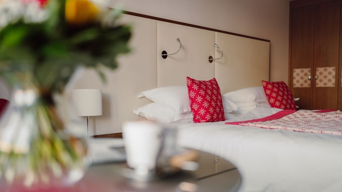 Flowers and coffee on table with cozy bed behind.