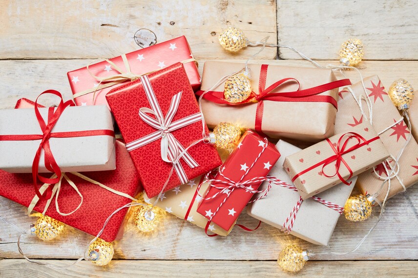 High angle view of a lot of wrapped Christmas gifts and strings lights on wooden background