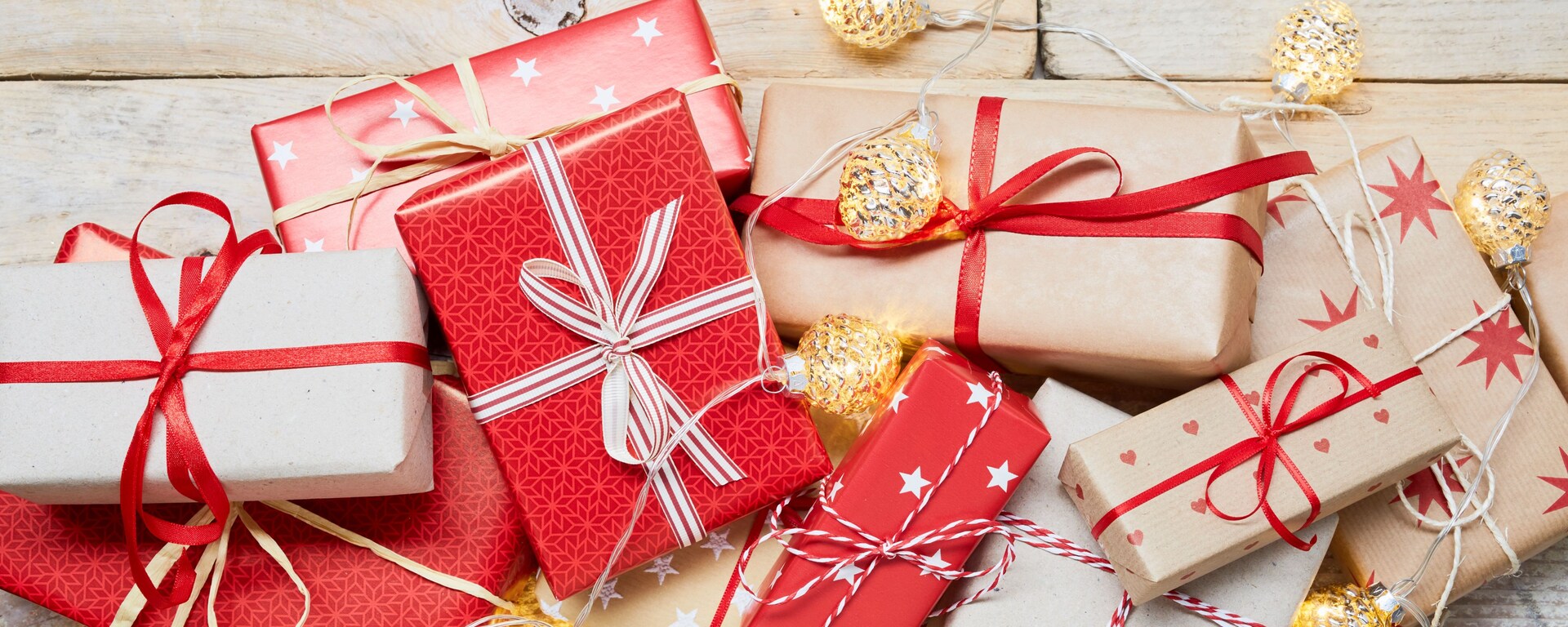 High angle view of a lot of wrapped Christmas gifts and strings lights on wooden background