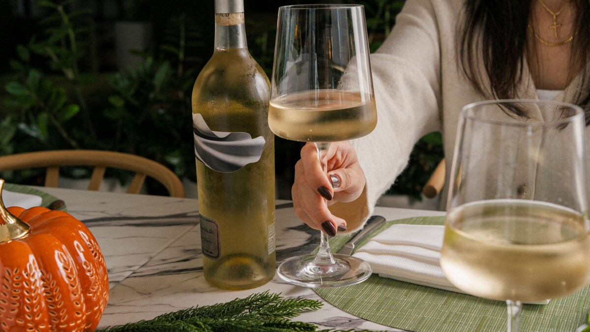Hand holding glass of white wine with wine bottle